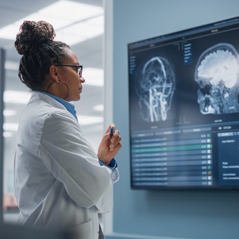 Medical Science Hospital: Confident Black Female Neurologist, Neuroscientist, Neurosurgeon, Looks at TV Screen with MRI Scan with Brain Images, Thinks about Sick Patient Treatment Method. Saving Lives